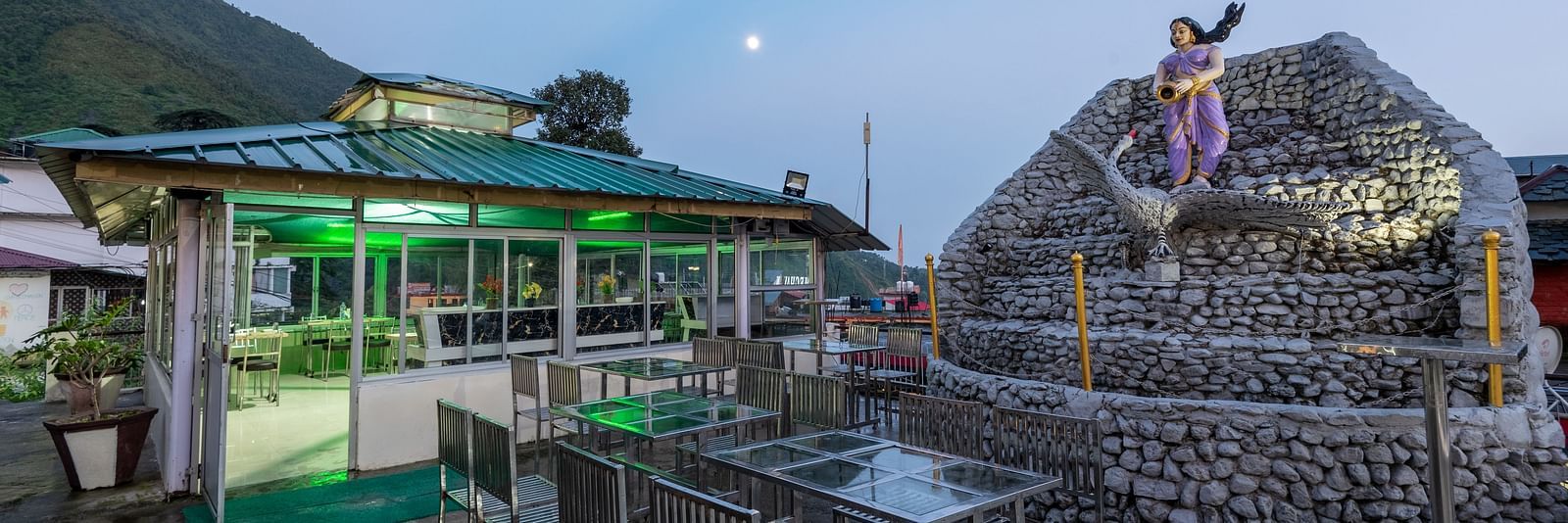 A view of an outdoor dining area at a resort with a stone fountain and a statue in the foreground -  DLS Meghavan Resort